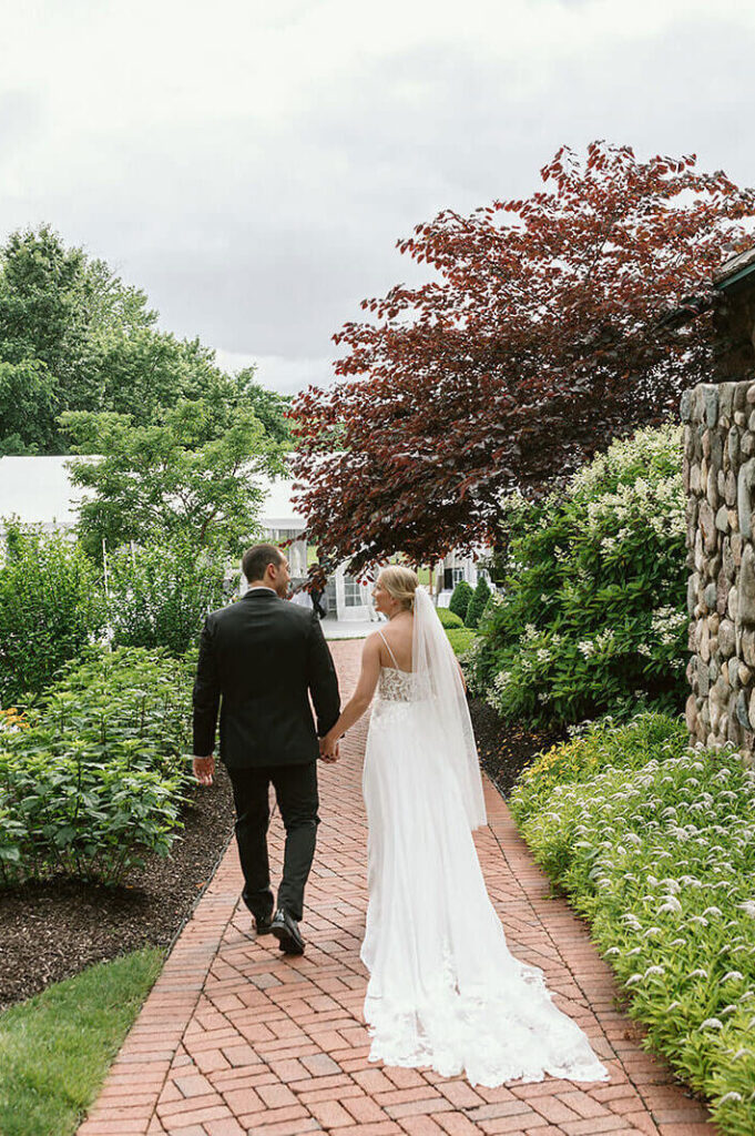 Bride and groom walking down cobble stone path, looking at each other.