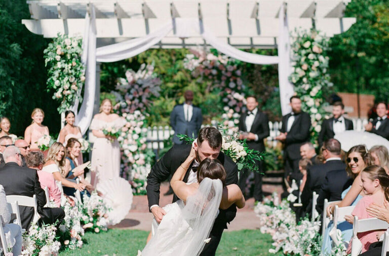 A groom dipping his bride while kissing her in the middle of the aisle.